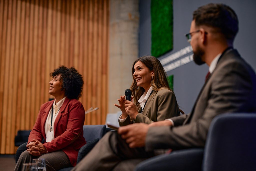 A businesswoman speaks on a panel to an audience at an event.