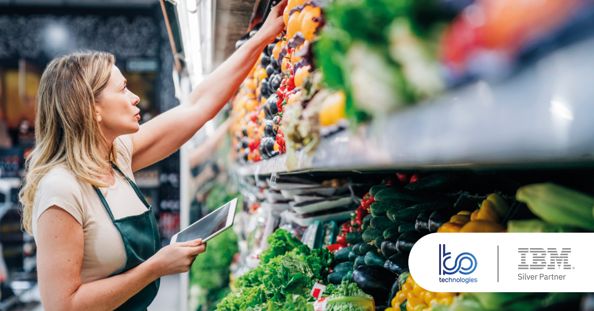 Main: A supermarket employee adjusts the vegetable section while holding an iPad. Inset: KO Technologies and IBM Silver Partner logos.