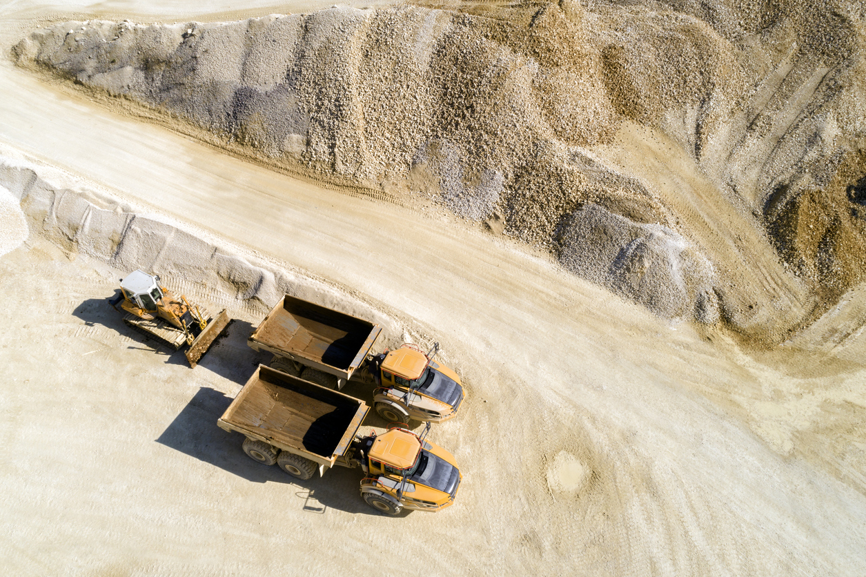 Aerial view of two dump trucks and a bulldozer in a quarry.