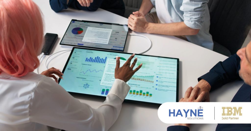 Main: A group discussion over a planning analytics dashboard. Inset: HAYNE Solutions and IBM Gold Partner logos.