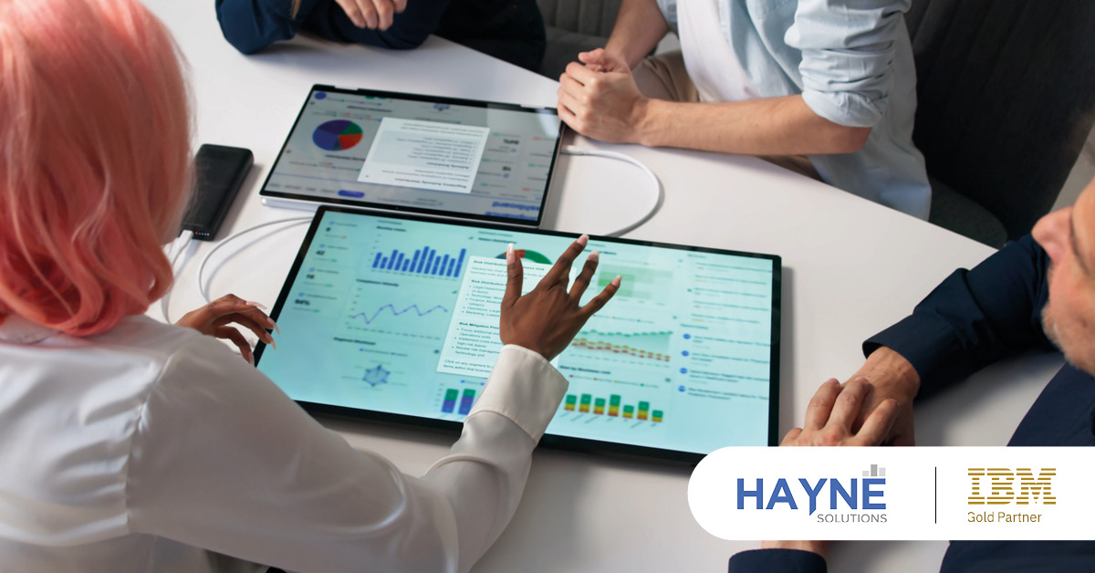 Main: A group discussion over a planning analytics dashboard. Inset: HAYNE Solutions and IBM Gold Partner logos.