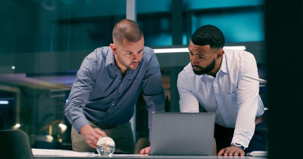 Two colleagues collaborate and review a piece of work on a laptop.